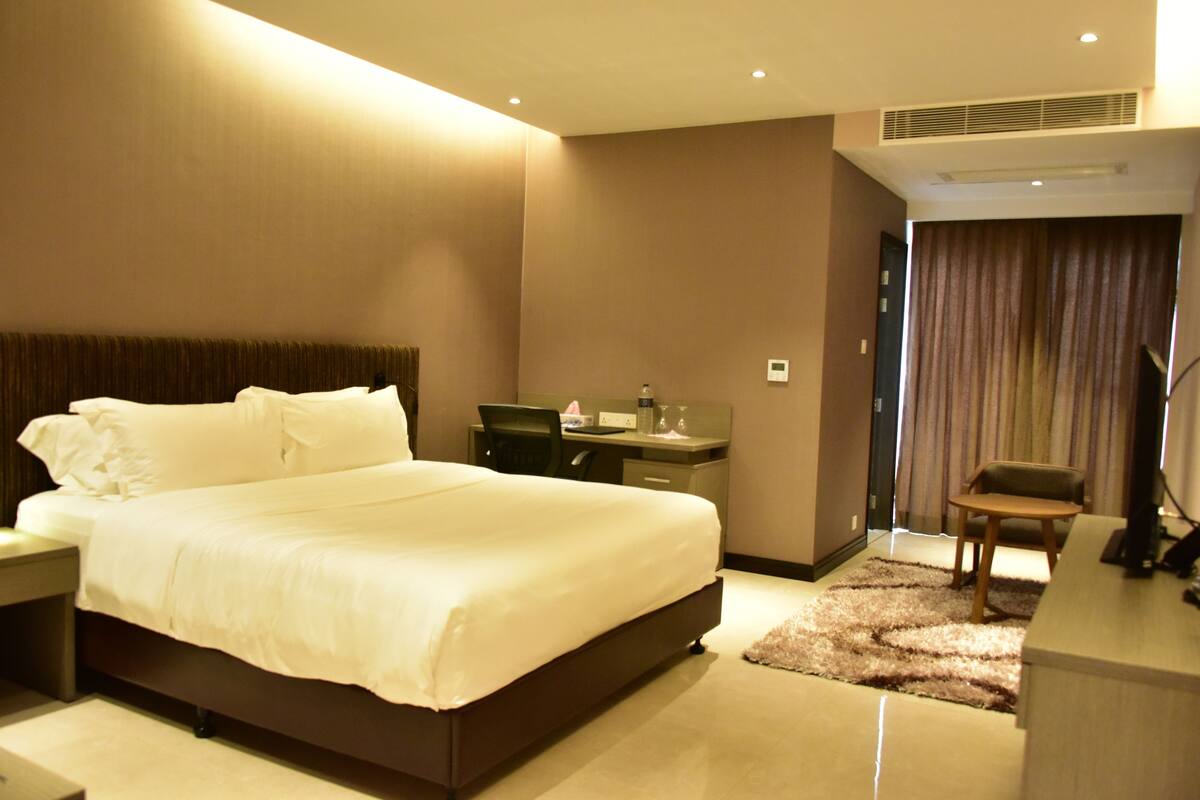 A hotel room with a large bed, a desk, a chair, and a TV.