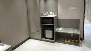 A modern hotel room with a built-in wardrobe, a small seating area, and a microwave. - Divine Center (Chowgacha)