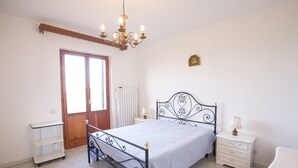 A bedroom with a bed, bedside tables, a chandelier, a radiator, and a door. - Villino Mediterraneo (Portoferraio)