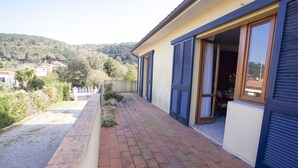A balcony with a brick floor, potted plants, and a view of a hillside. - Villino Mediterraneo (Portoferraio)