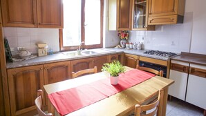 A kitchen with wooden cabinets, a sink, a stove, and a dining table with chairs. - Villino Mediterraneo (Portoferraio)