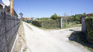 A rural road with a metal fence on one side, a dirt path, and a gate leading to a property with a satellite dish and a small building. - Appartamento il Mandarino (Portoferraio)