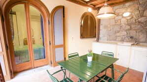 A dining area with a green table and chairs, a potted plant, and a stone wall.