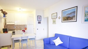 A modern living room with a blue sofa and a dining area with a white table and chairs.