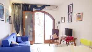 A living room with a blue sofa, a white table with a vase of flowers, a television, and a wooden chair.