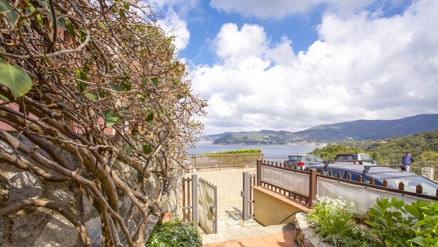 A coastal pathway with a stone wall, a metal gate, and a view of the sea and mountains.