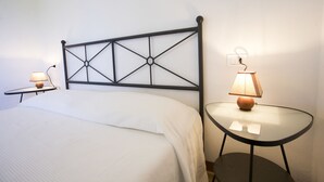 Cama bem arrumada com cabeceira, duas mesas de cabeceira com abajures e uma tomada na parede.