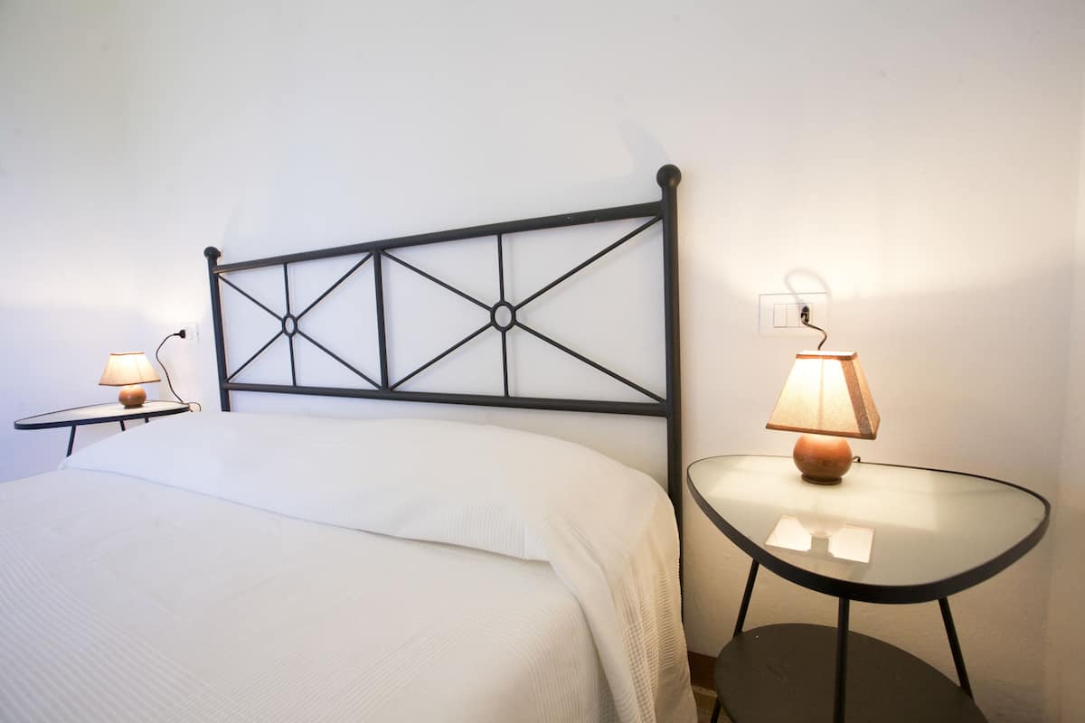Un lit bien fait, avec une tête de lit, deux tables de chevet avec des lampes et une prise électrique au mur.