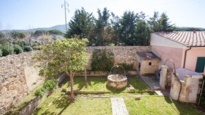 Um pátio com muro de pedra, uma árvore, um poço e um pequeno edifício com telhado de telhas.