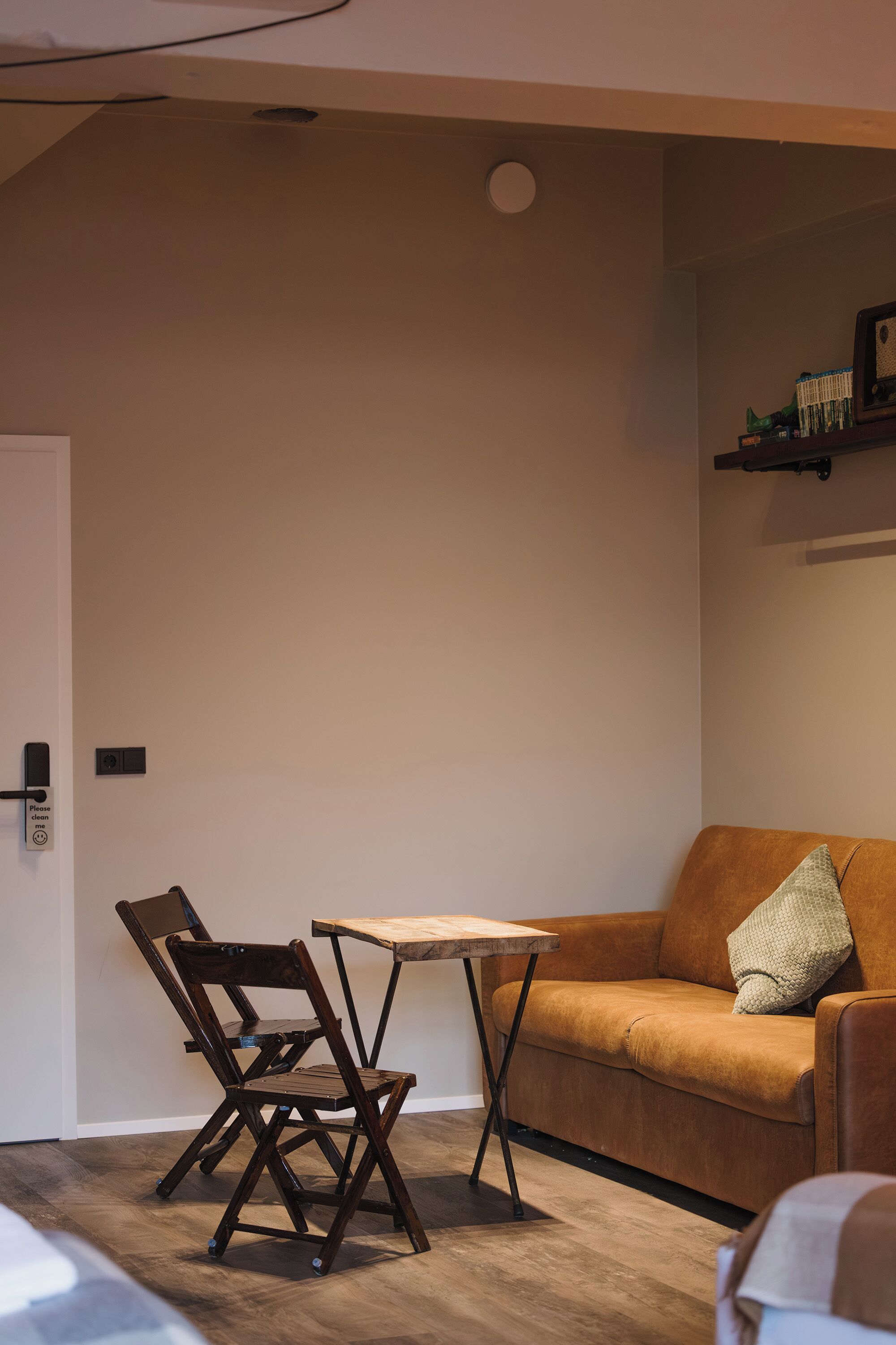 Una habitación con una mesa de madera, un sofá marrón y una silla. Hay una estantería con libros y un cuadro en la pared.