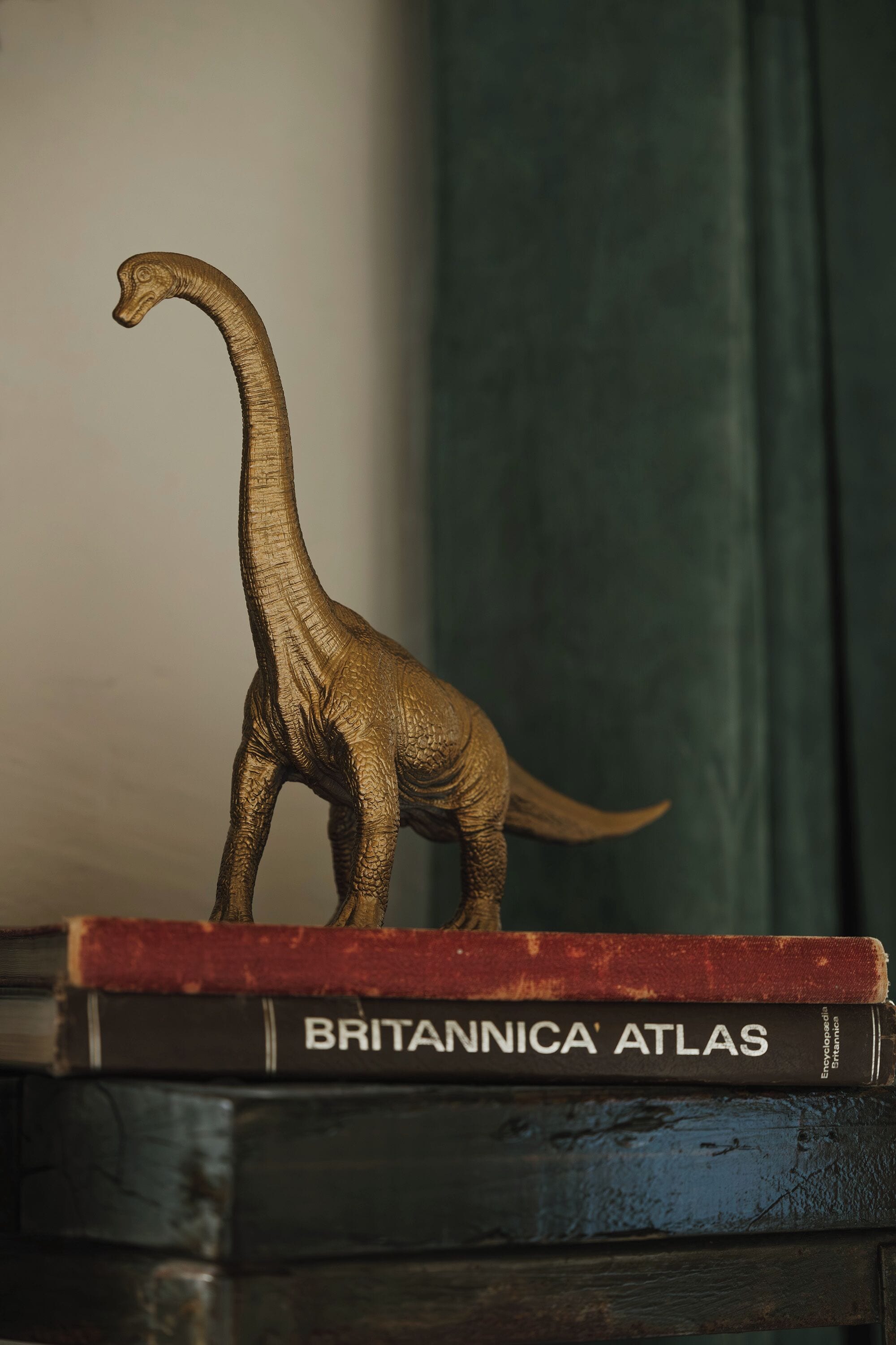 A model of a dinosaur on top of a book titled 'BRITANNICA ATLAS'.