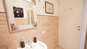 A bathroom with a white sink, a mirror with a distressed frame, beige tiles, a framed welcome sign, and a door.