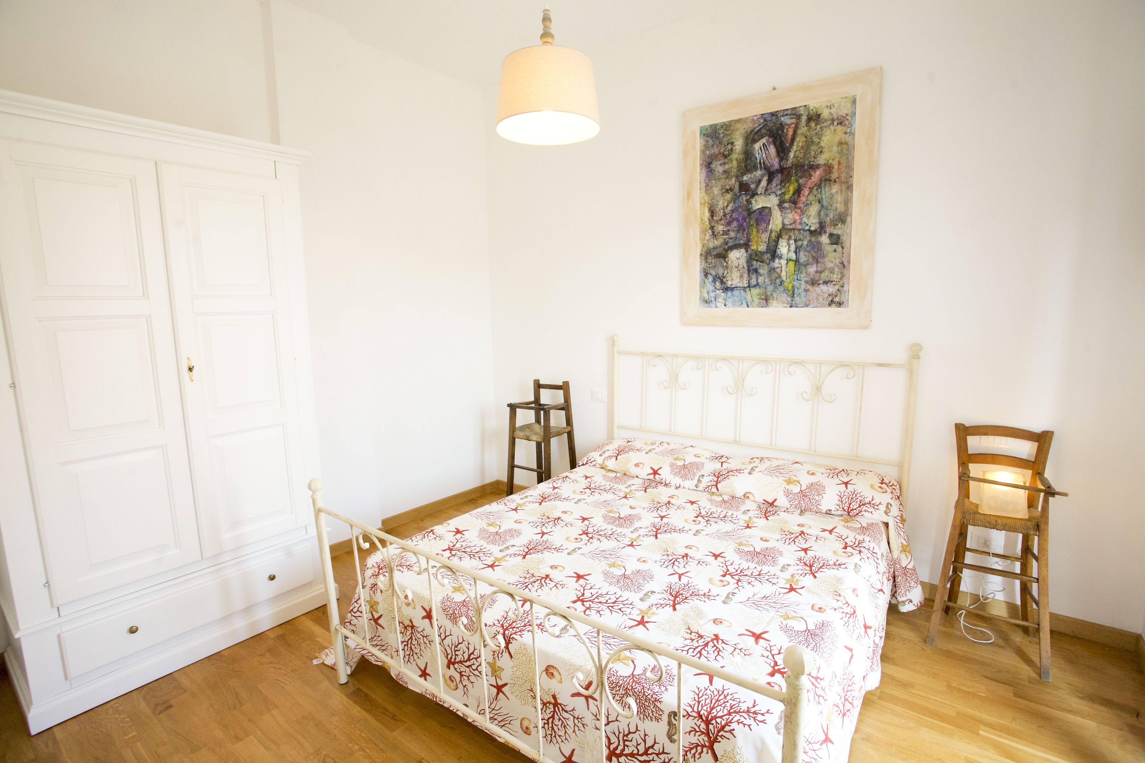 Une chambre à coucher avec un lit, deux chaises, une armoire et un tableau accroché au mur.
