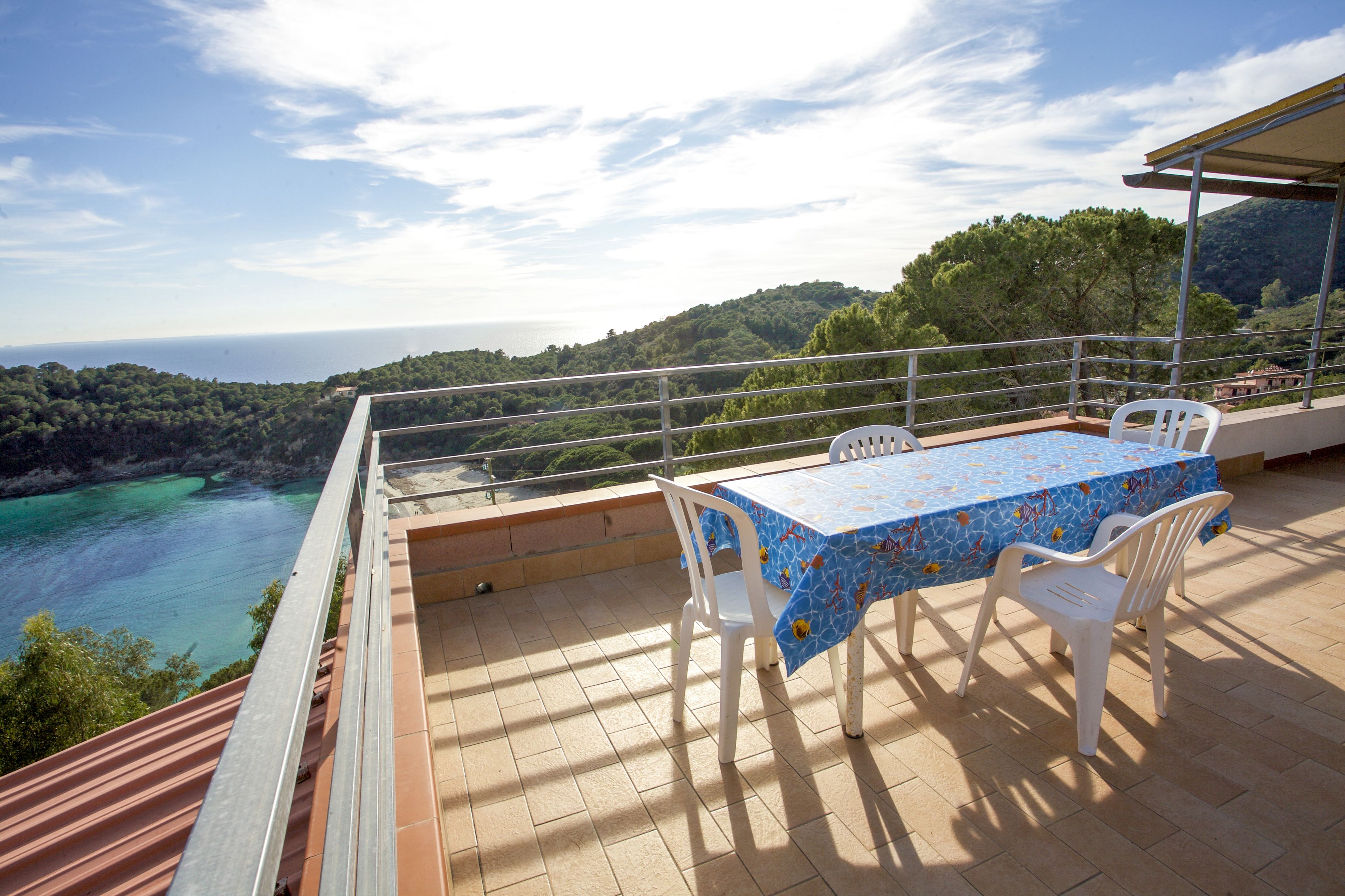A terrace with a table and chairs, overlooking a coastal landscape.