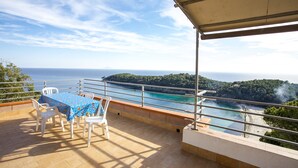 Un balcon avec une table et des chaises, offrant une vue sur la côte, avec une eau turquoise et une plage.