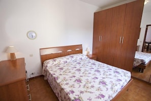 Un dormitorio con una cama de madera, una mesita de noche, un armario y una pequeña mesa con lámpara.