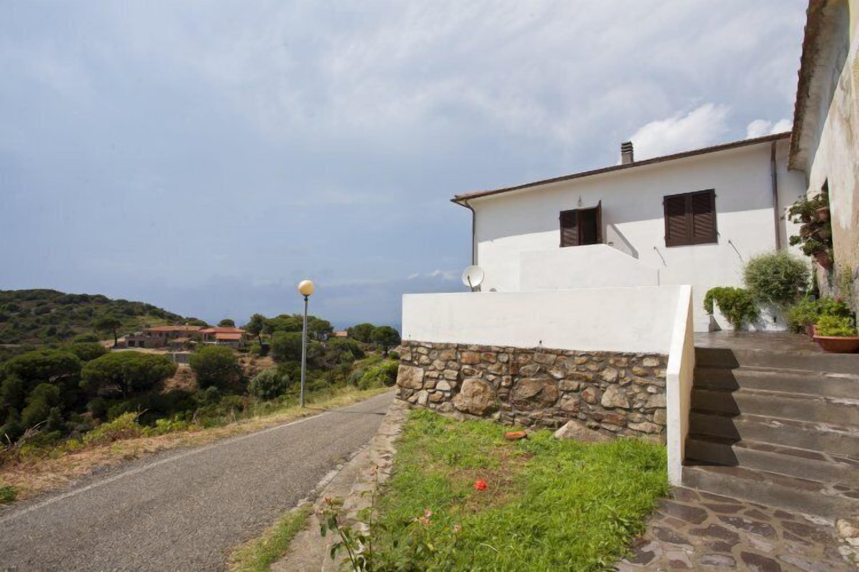 A white building with a stone wall and a paved path leading to the entrance.
