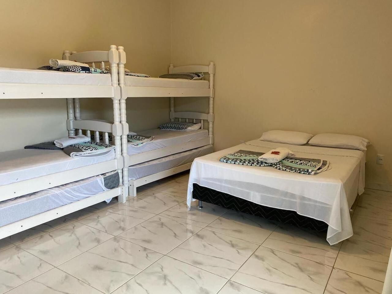 A room with two bunk beds and a single bed, all with white bedding.