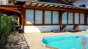 Una piscina con sillas de descanso, un porche cubierto y vistas a un edificio con amplios ventanales.