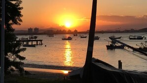Atardecer sobre un cuerpo de agua con barcos, una palmera y un muelle.