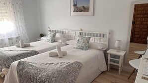Habitación de hotel con dos camas, una mesita de noche con lámpara, un cuadro enmarcado en la pared y una puerta de madera.