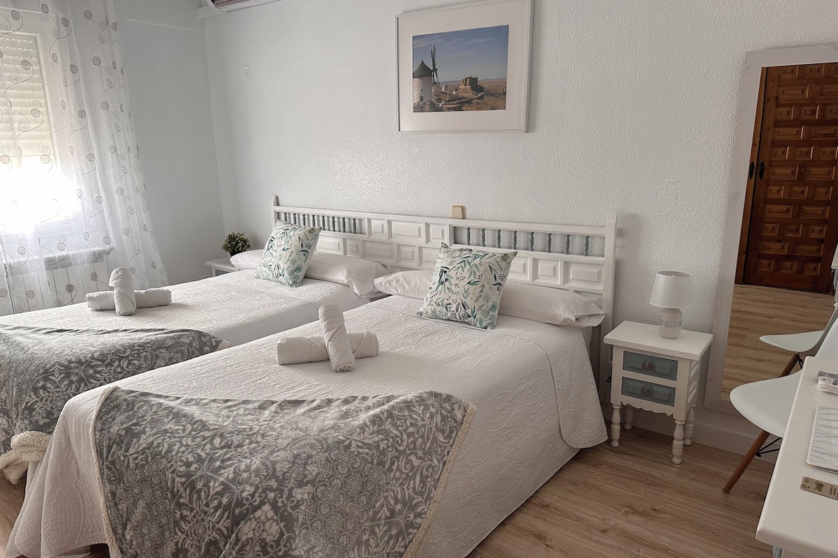 A hotel room with two beds, a small bedside table with a lamp, a framed picture on the wall, and a wooden door.