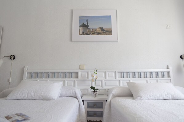 Habitación de hotel con dos camas, cabecera blanca, un cuadro en la pared y una pequeña mesa con una orquídea.