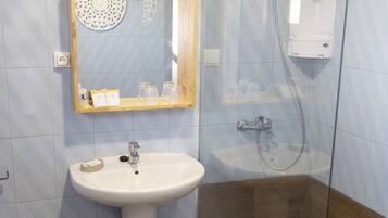 A bathroom with a pedestal sink, a glass shower enclosure, and a mirror with a decorative frame.