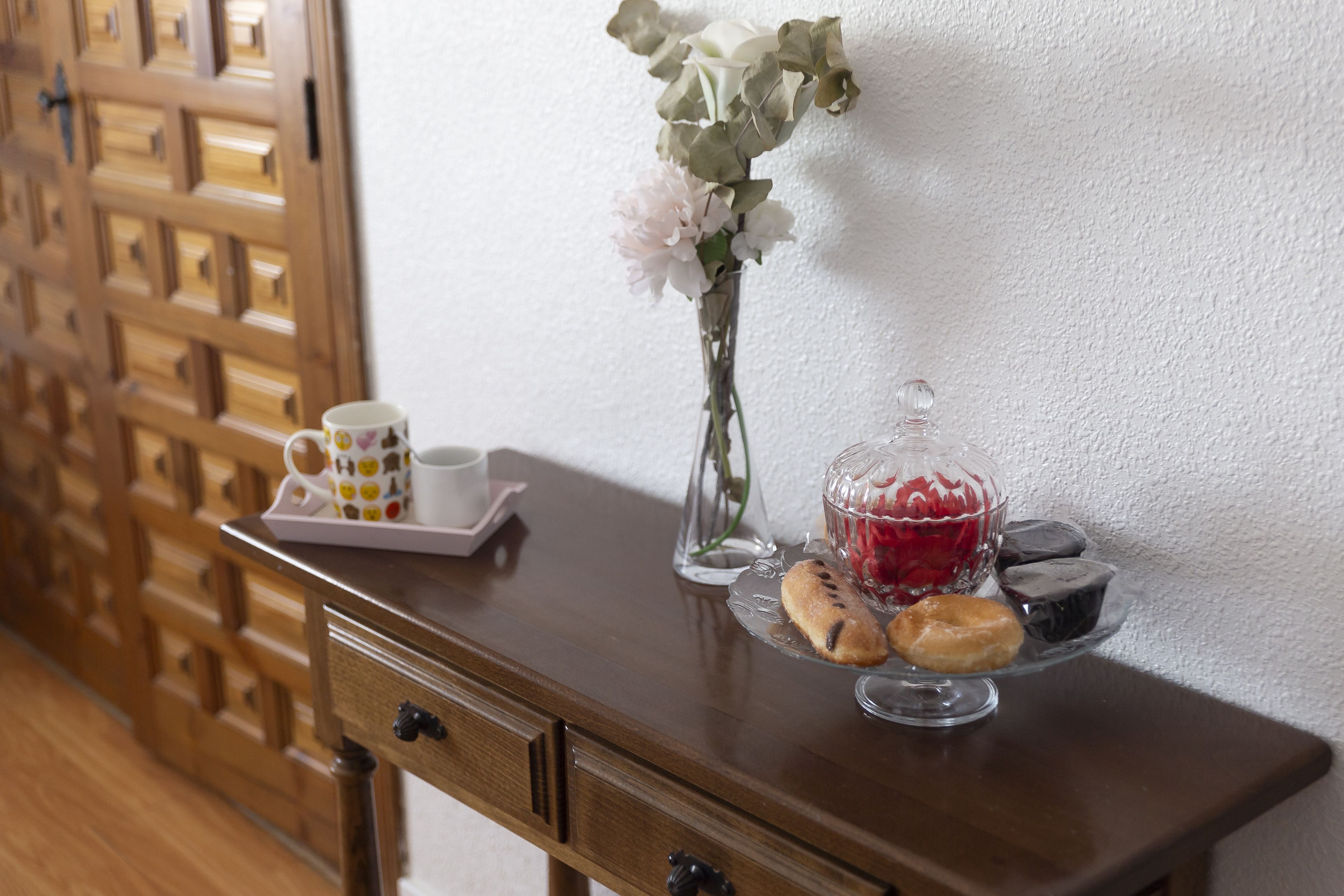 Ein Holztisch mit einer Etagere voller Gebäck, einer Glasvase mit Blumen und einer Tasse mit Untertasse.
