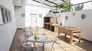 Un patio exterior con mesa de fútbol de mesa, un horno de ladrillo y una zona de comedor con sillas y una mesa.