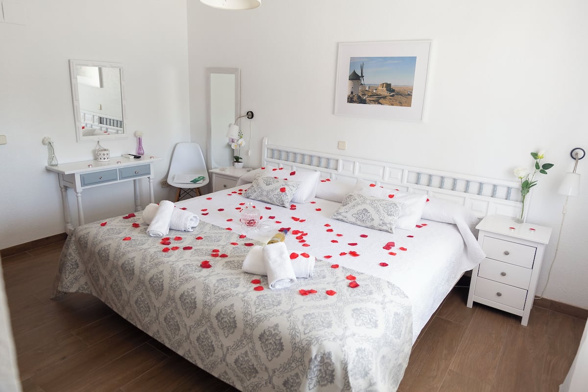A neatly arranged hotel room with a large bed, a bedside table, a chair, a desk, and a mirror.