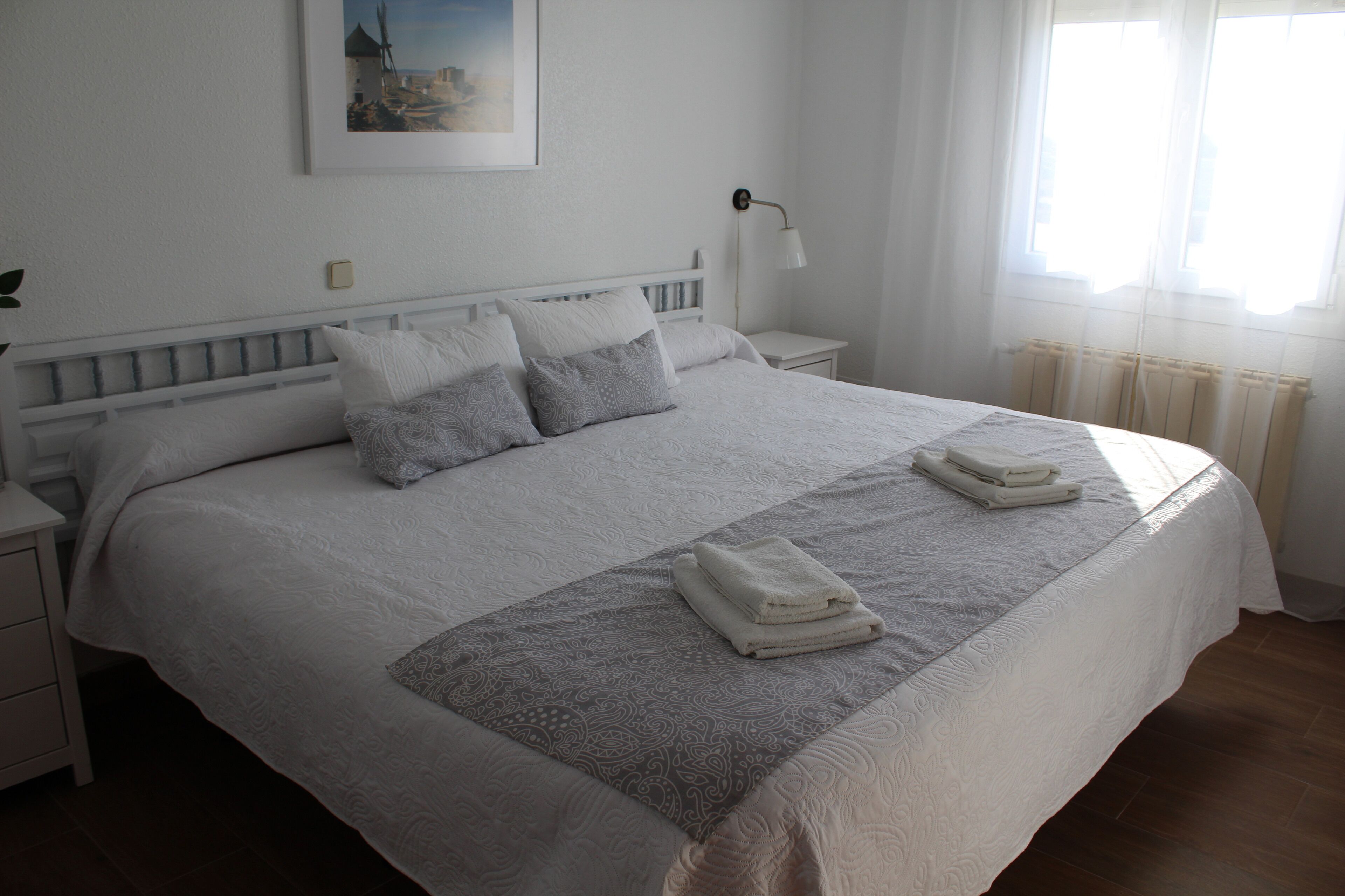 Una cama bien hecha con un edredón estampado y almohadas, una mesita de noche con una lámpara y un cuadro en la pared.