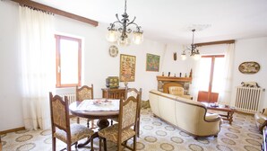 Ein Essbereich mit rundem Tisch, Stühlen und einer Couch. Es gibt eine Chandelier, einen Kamin und ein Fenster mit Vorhängen.