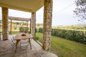 An outdoor patio with stone pillars, a wooden table, and white chairs.
