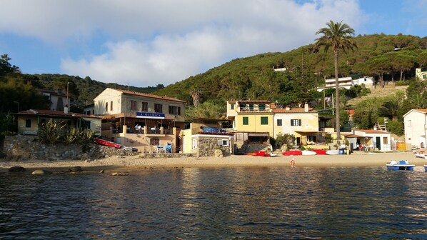 A coastal building named 'L'Ostrica' with a stone facade, a balcony, and a view of the sea.