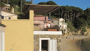 A coastal building with a stone facade, a balcony with flowers, and a beach in the background. - Appartamento Il Sottomarino (Portoferraio)