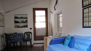 A room with a wooden floor, a blue sofa, a dining table with chairs, and a door with a window. - Appartamento Il Sottomarino (Portoferraio)