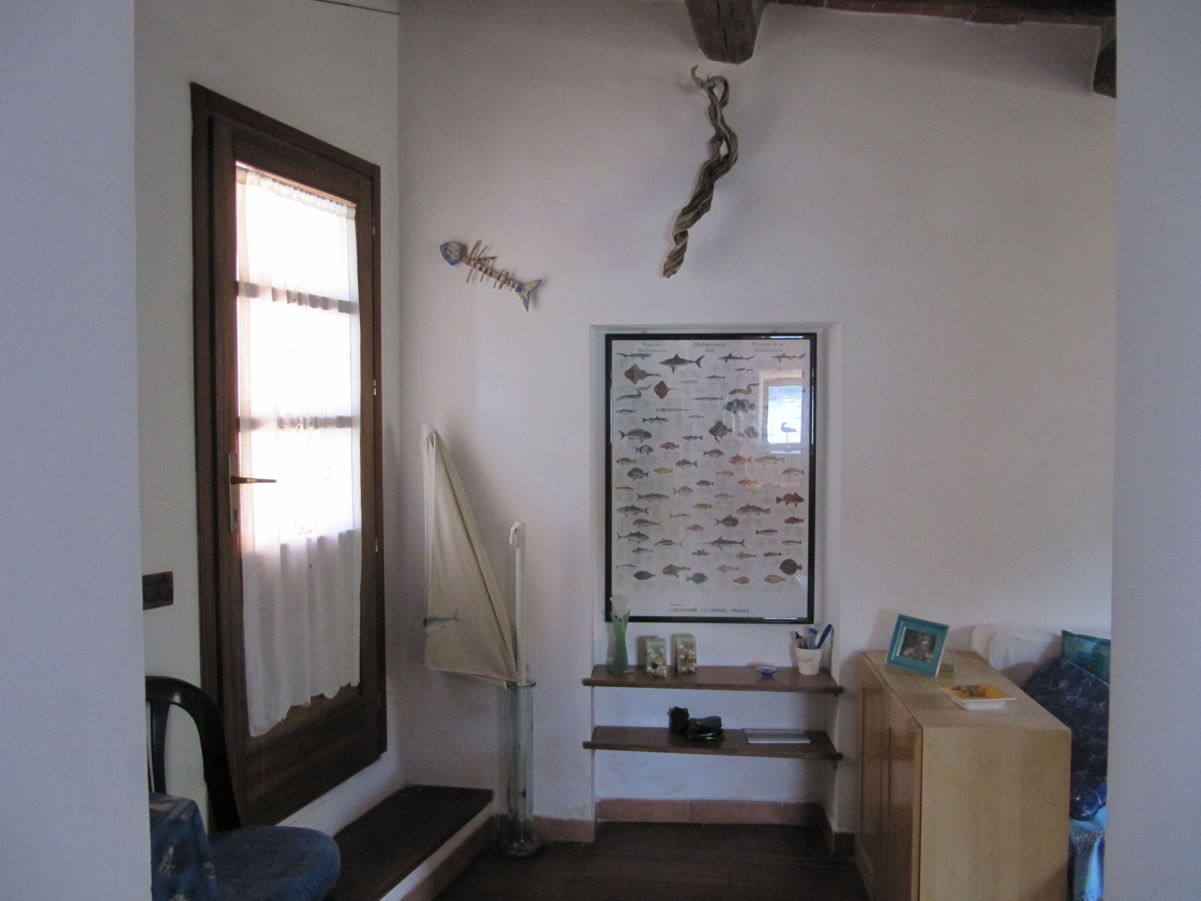Um quarto com porta de madeira, um painel decorativo com peixes na parede, uma luminária e uma pequena mesa com um porta-retrato.