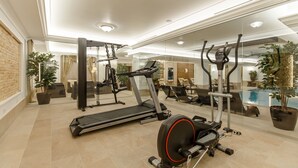 Une salle de sport moderne équipée d’un tapis de course, d’un vélo elliptique et d’appareils de musculation, de grands miroirs et d’une piscine visible à travers les murs de verre.