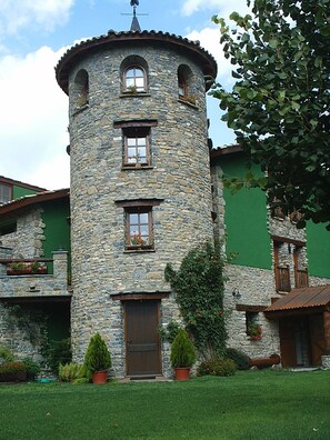 A stone tower with a central door and windows, surrounded by a well-maintained lawn and potted plants.