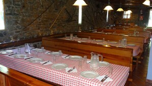 Un restaurant avec des bancs et des tables en bois, des assiettes blanches, des couverts et des verres transparents.
