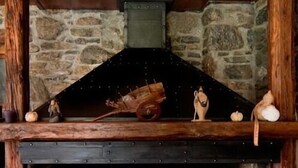 Une cheminée en pierre avec un manteau en bois, présentant un style rustique agrémenté d’une grille en métal et d’objets décoratifs.