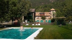 Une piscine dans laquelle une personne plonge, entourée d’une zone herbeuse et d’un bâtiment doté d’une tour.