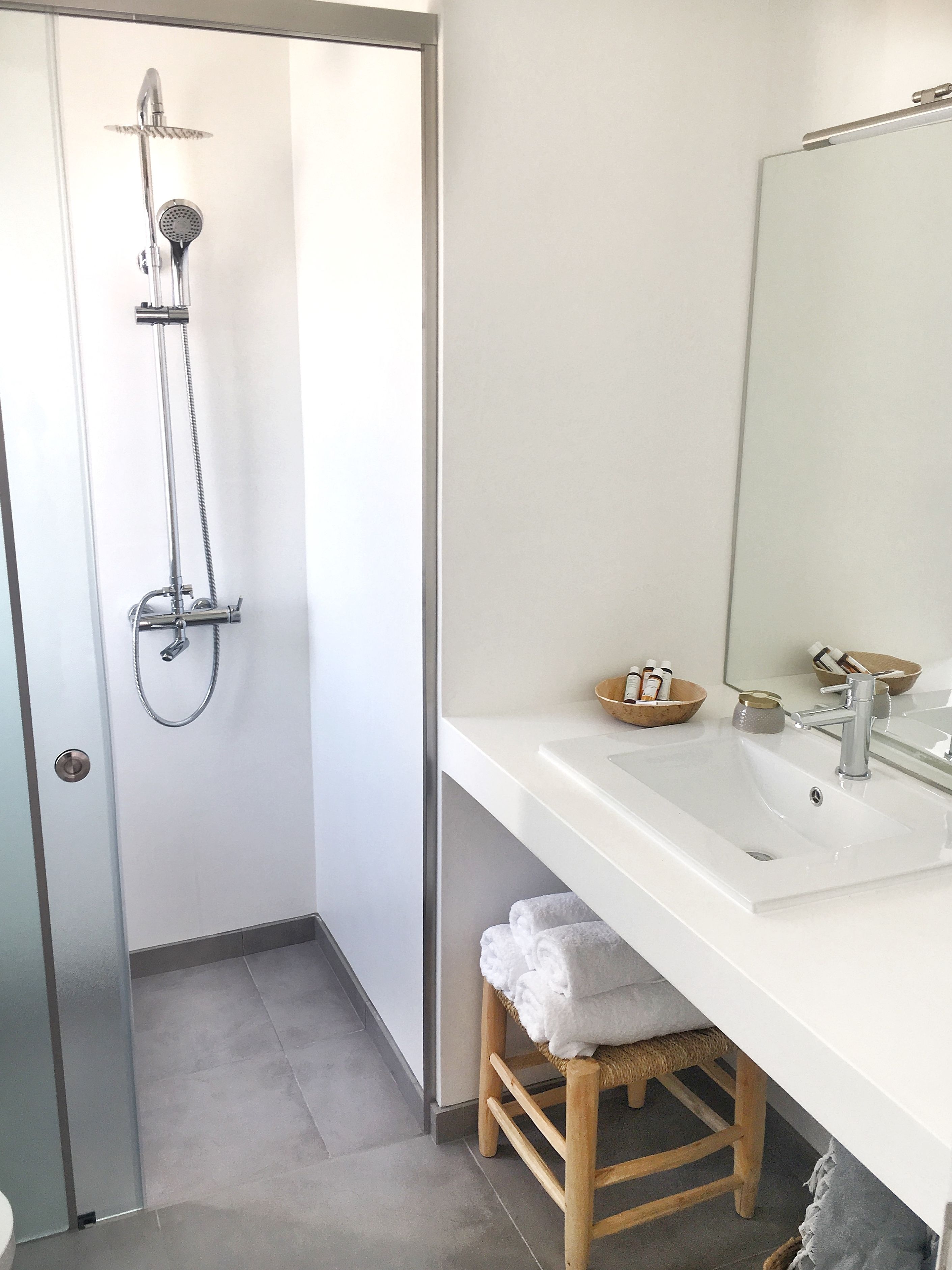 Un baño con ducha, lavamanos, espejo y un taburete con toallas.