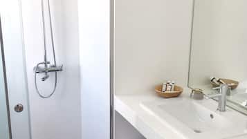 Un baño con ducha, lavamanos, espejo y un taburete con toallas.