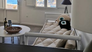 Un dormitorio con una cama, una lámpara, un ventanal con contraventanas, una mesita con una cesta y una botella.