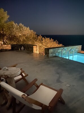 Zona de piscina exterior con muros de piedra y vista al mar de noche.