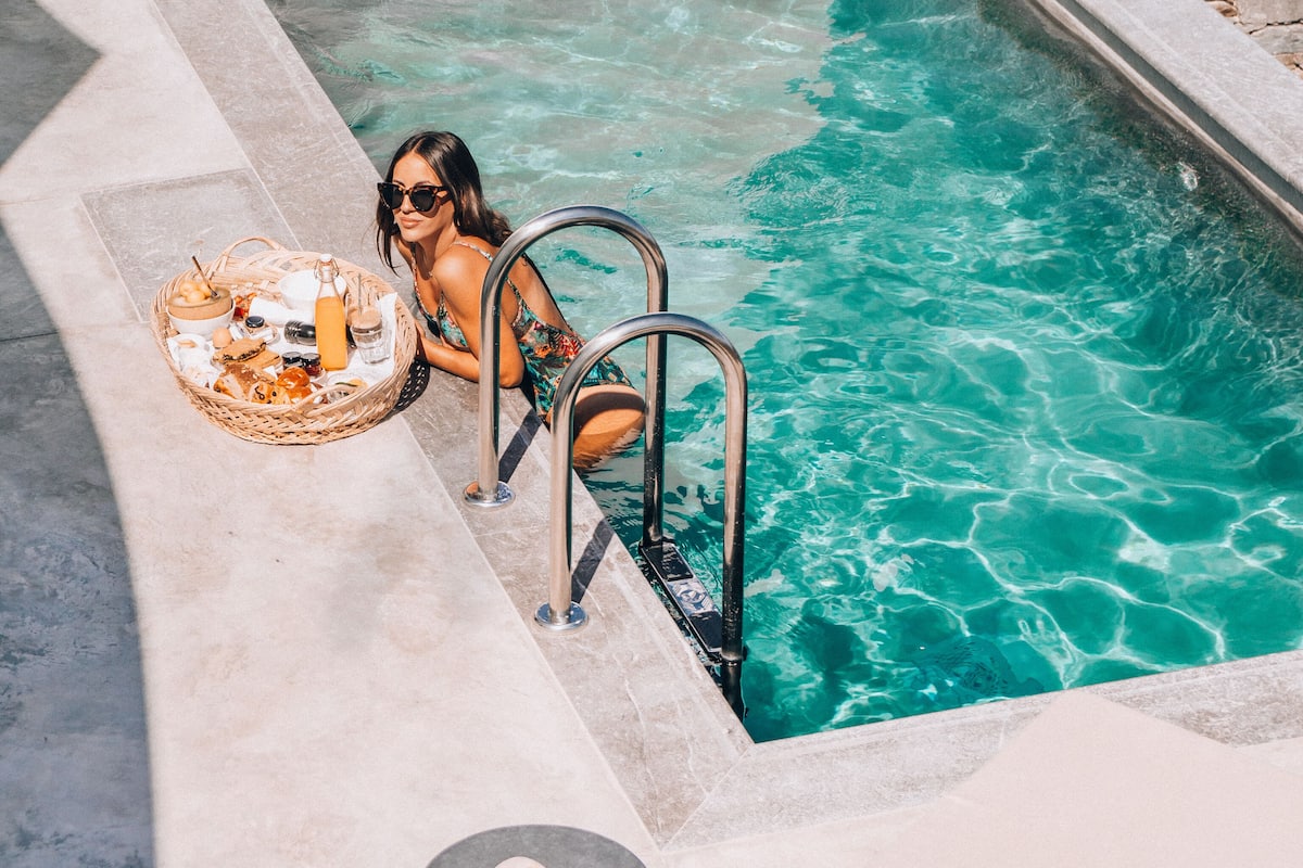 A pool area with a stone border, a wicker basket with food, and a lounge chair.