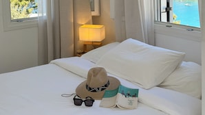 Una habitación de hotel con una cama, una mesita de noche con una lámpara, un sombrero, gafas y un libro.