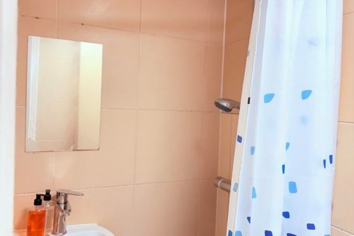 A bathroom with a white sink, two bottles of liquid soap, a mirror, and a shower curtain with blue polka dots.